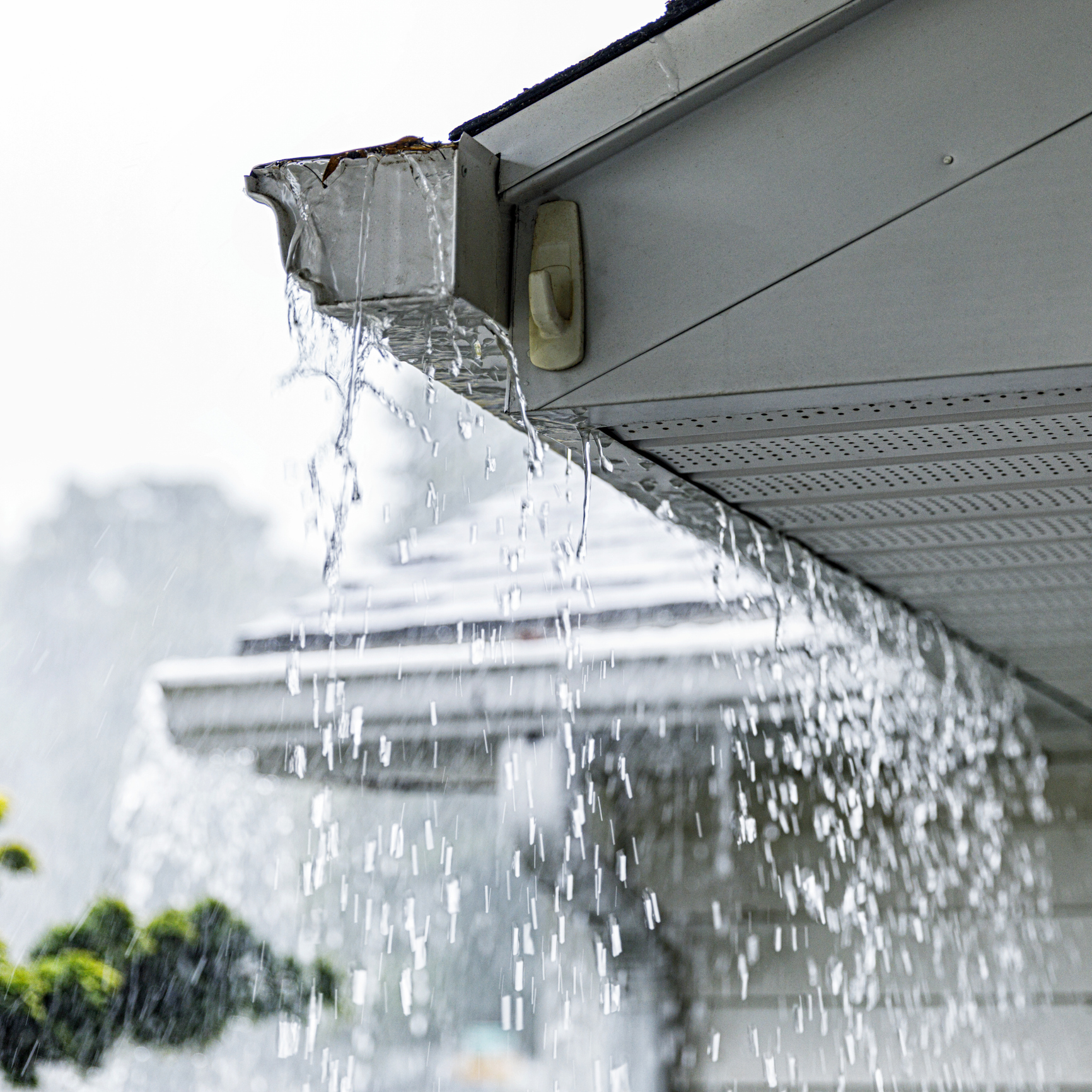 Drenching downpour rain storm water is overflowing off the tile shingle roof - streaming and splashing over the eaves trough aluminum roof gutters on a suburban residential colonial style house near Rochester, New York State, during a torrential mid-summer July downpour.